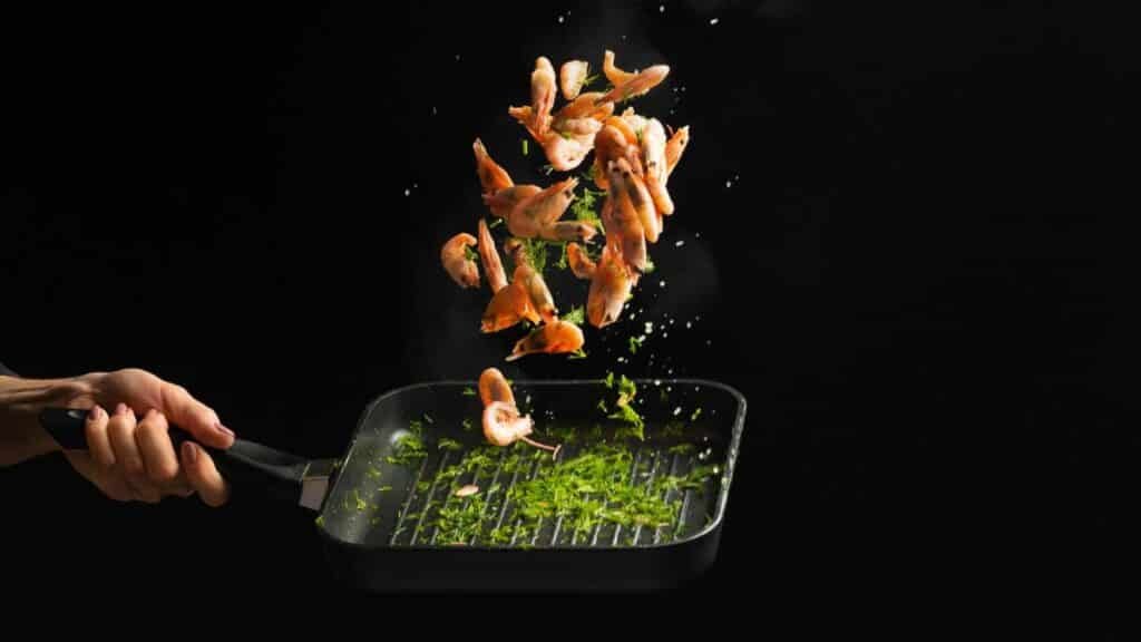 a chef flipping shrimp in a pan