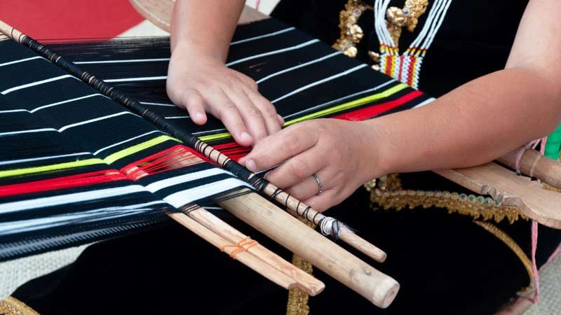 a woman patiently weaving on a loom